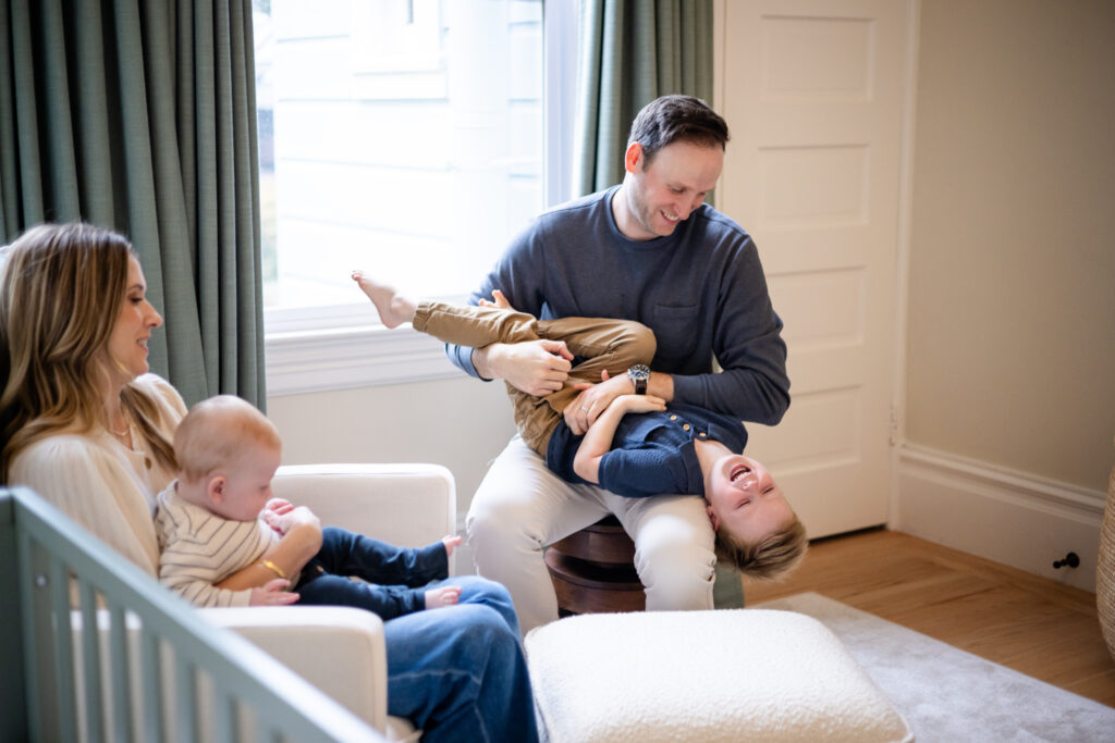 mom holding baby in chair, dad tickline toddler near window